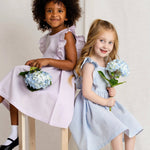 Two young girls in dresses holding flowers against a plain background