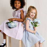Two young girls in dresses holding flowers against a plain background