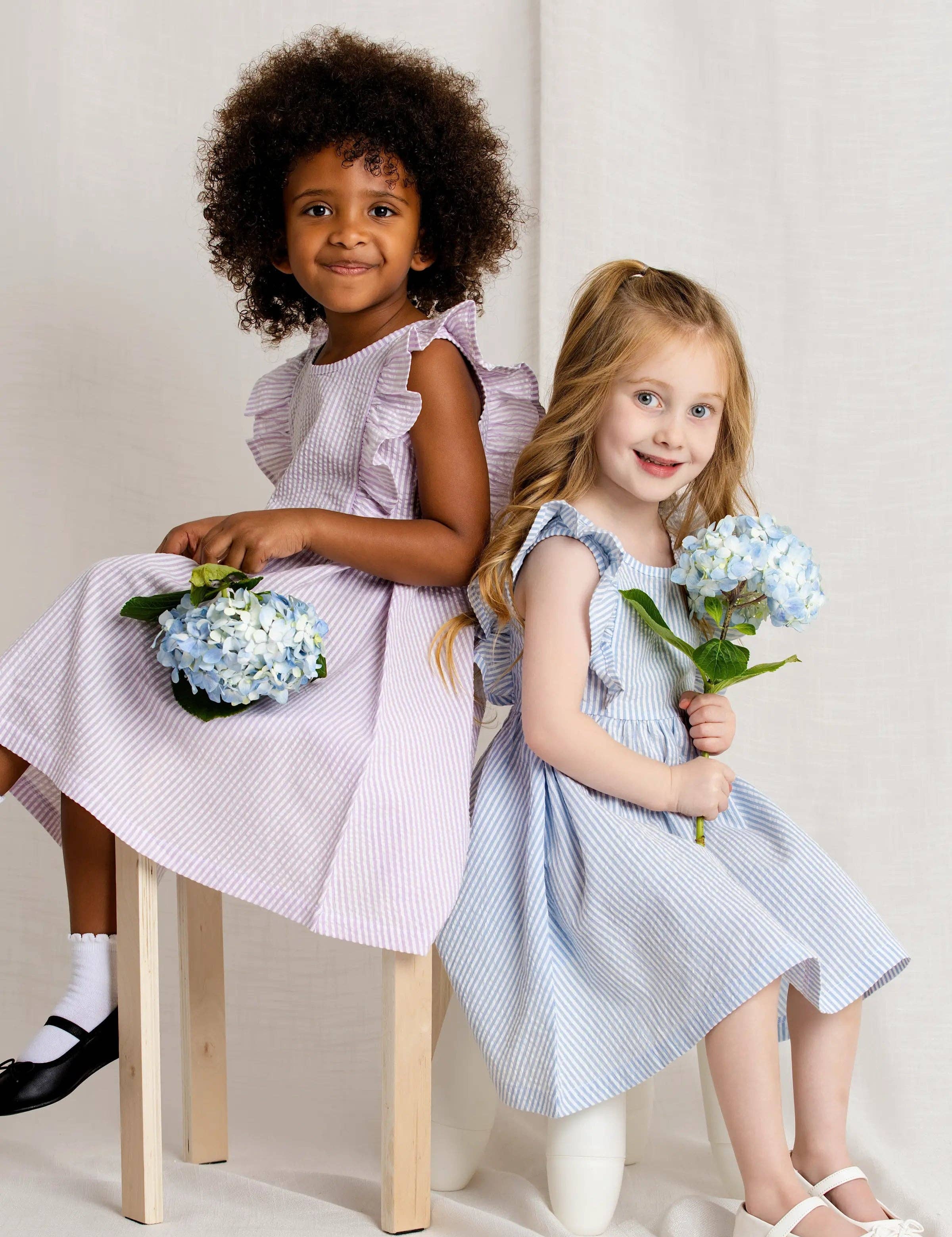 Two young girls in dresses holding flowers against a plain background