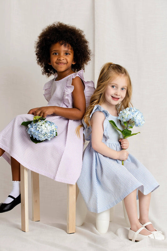 Two young girls in dresses holding flowers against a plain background