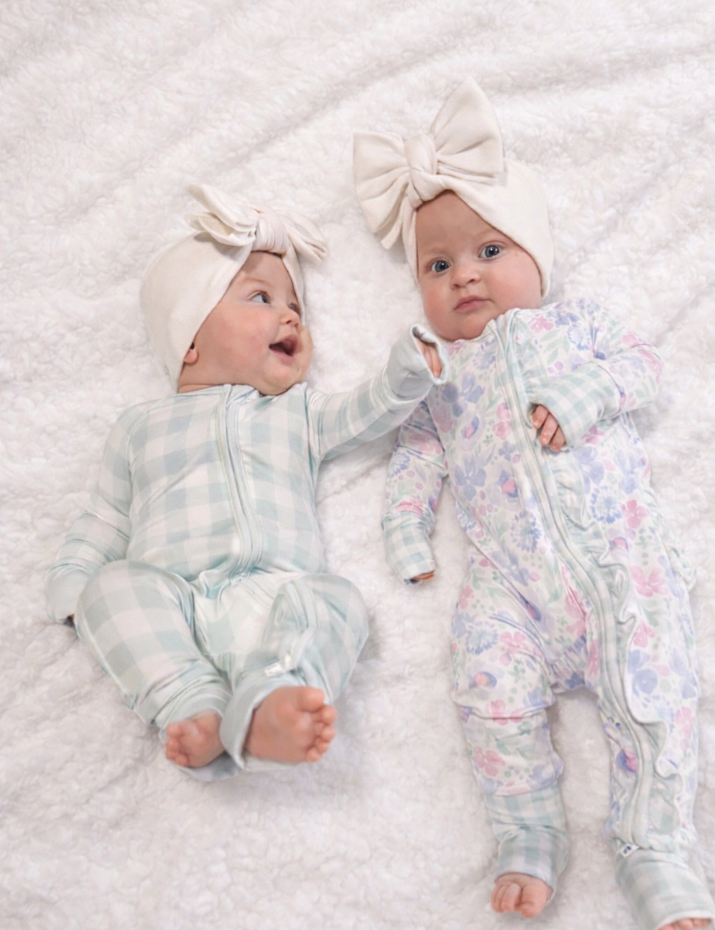 Two babies wearing floral outfits and headbands lying on a textured white surface.